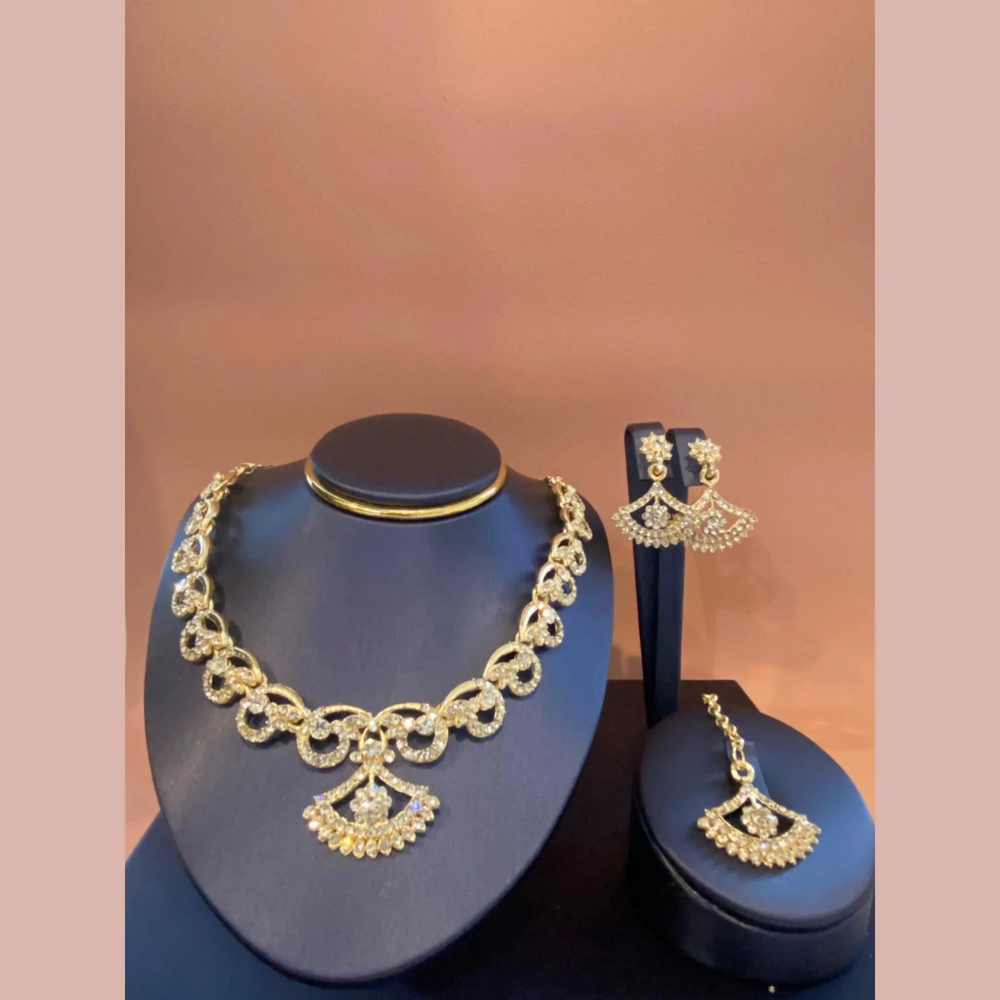 Gold necklace and earrings on blue stands against a brown background